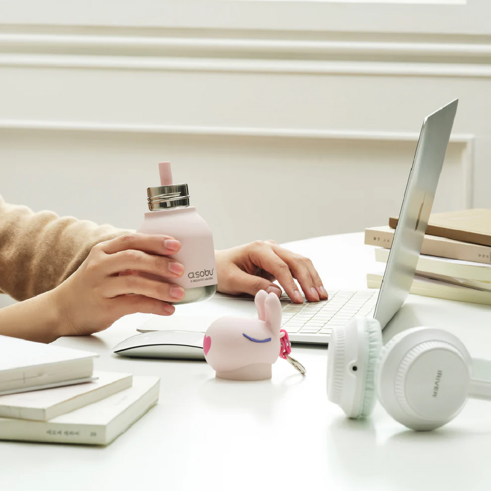 Person using a laptop with a pink water bottle and white headphones on a desk.