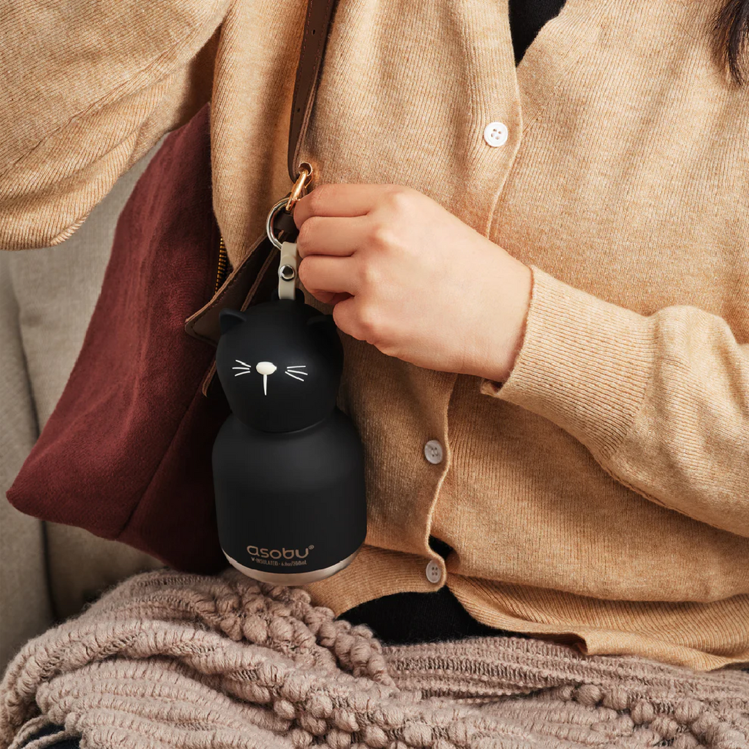 Person holding a black insulated bottle with a cat design, wearing a beige jacket.