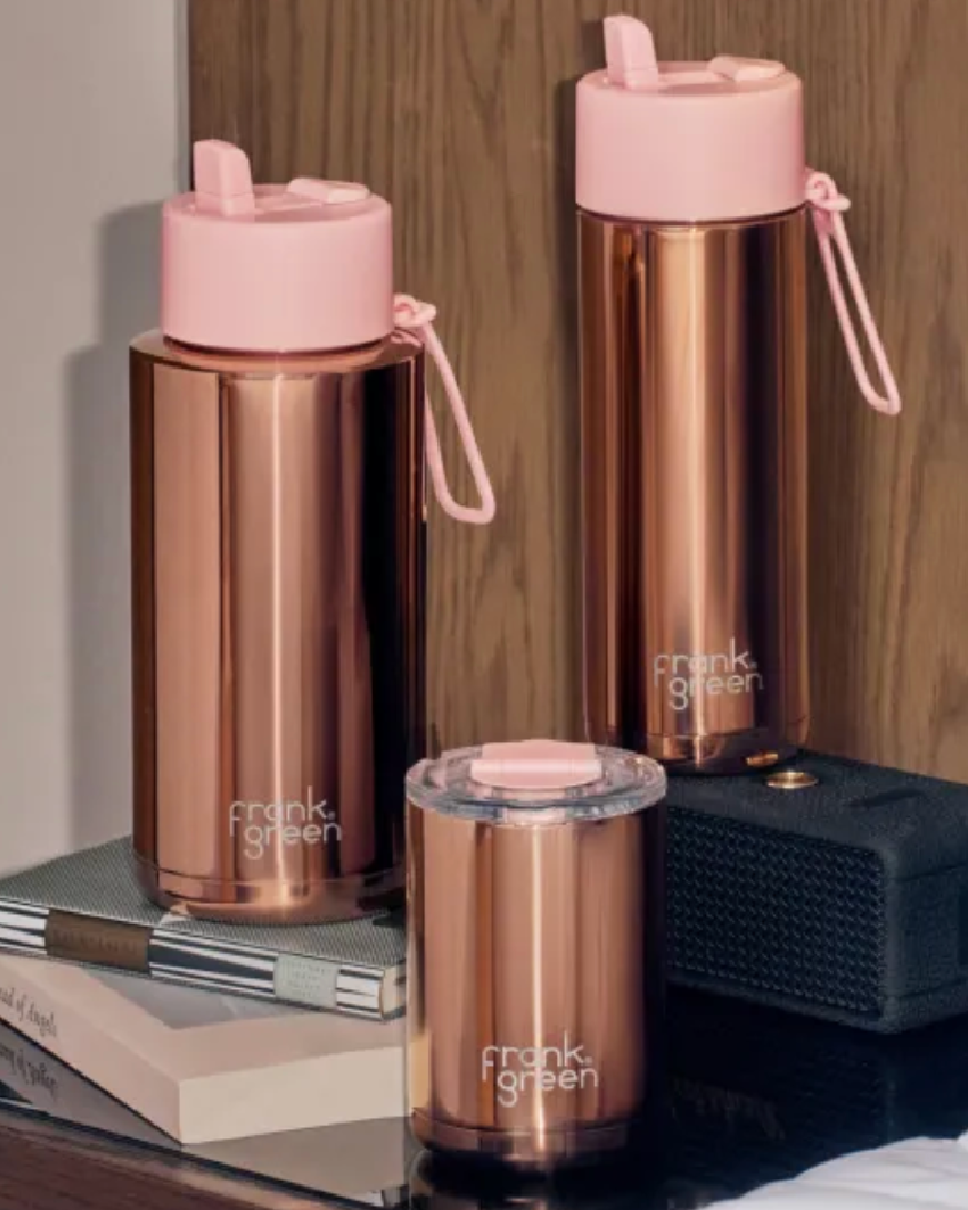 Set of rose gold water bottles with pink lids on a wooden surface.