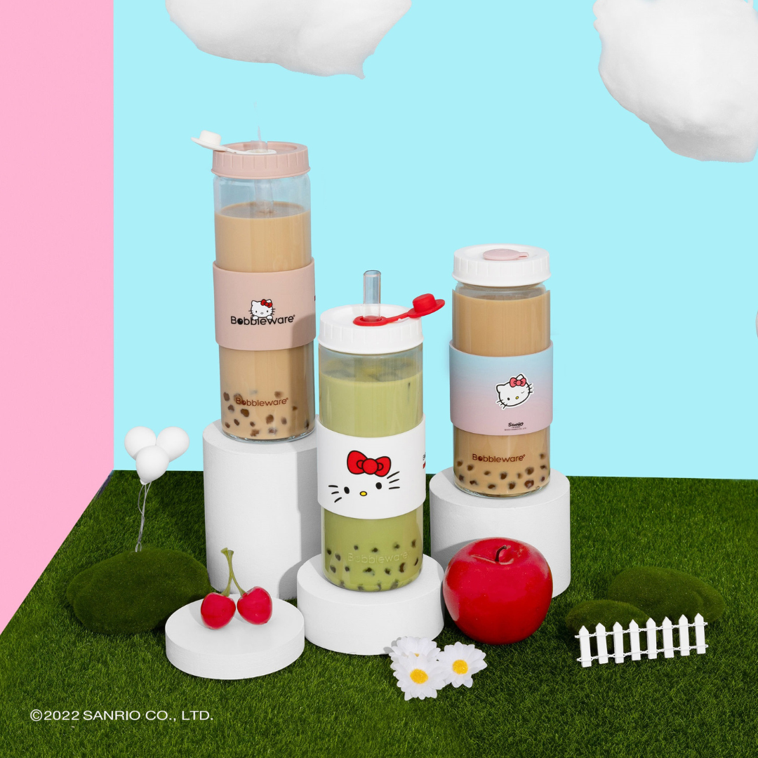 Hello Kitty-themed bubble tea set with colorful drinks on a grassy patch with pink and blue background