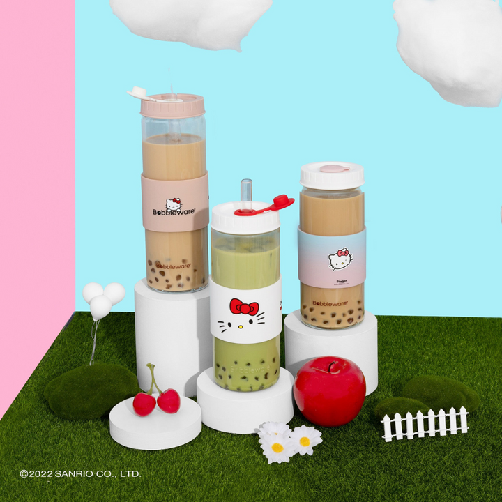 Hello Kitty-themed bubble tea set with colorful drinks on a grassy patch with pink and blue background